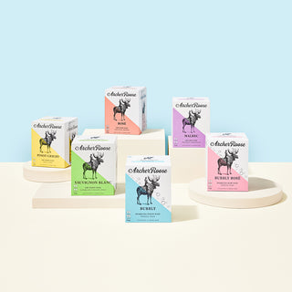 Archer Roose Wine Four Packs on a cream surface at different heights with a baby blue background | Archer Roose Wines | Wine in a Can | Canned Wine | Luxury Wine. In Cans | Still Wine | Sparkling Wine | White Wine | Rose Wine | Red Wine